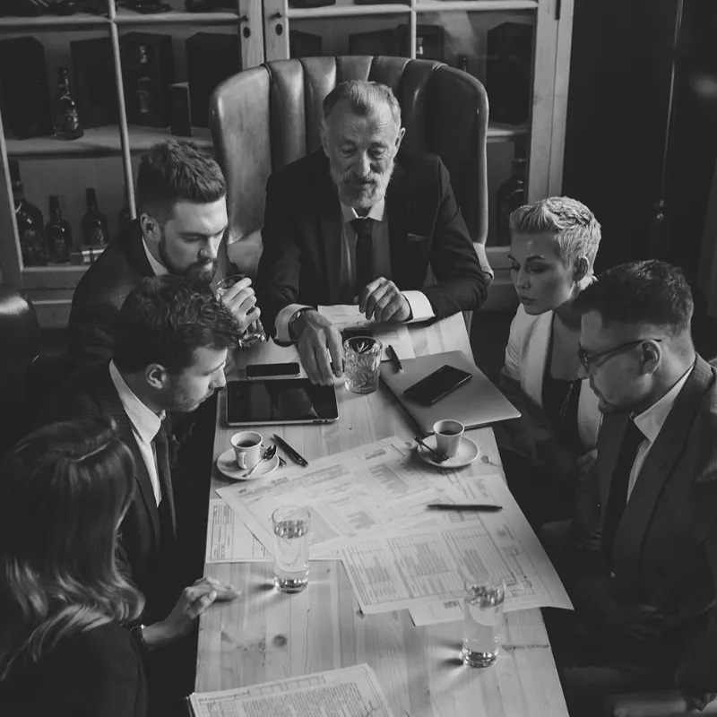 Nat Manz Business Defined - executives in formal attire reviewing strategy documents during a high-level business meeting.