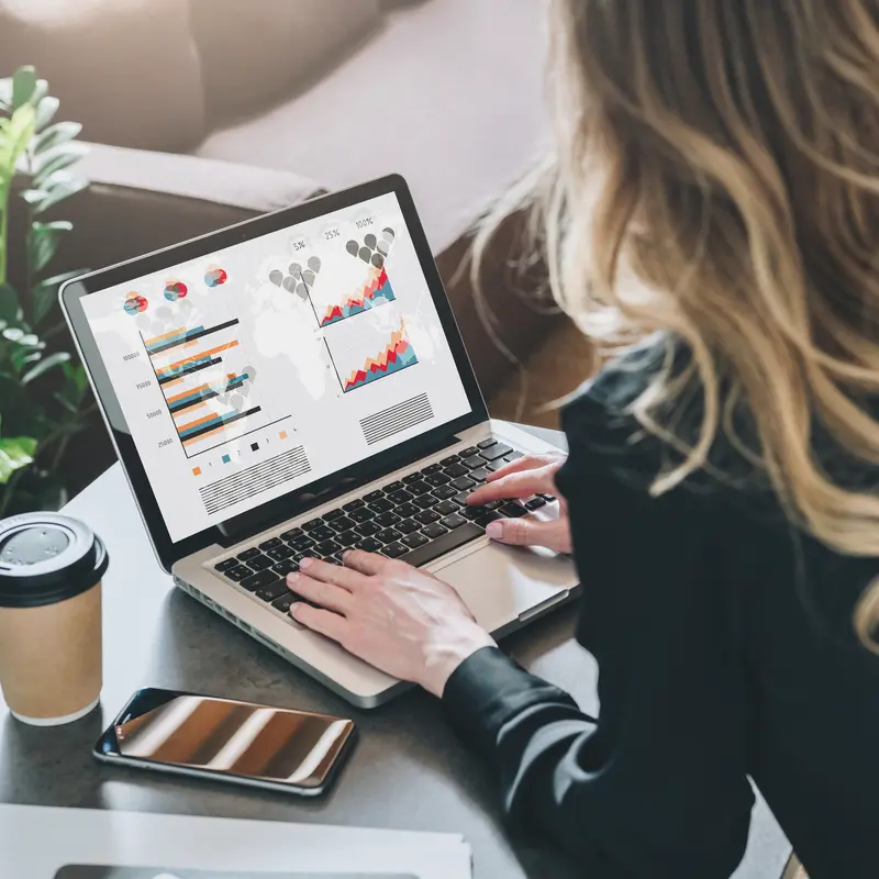 Woman analyzing charts on laptop with coffee and smartphone nearby, concept for online reputation marketing, performance tracking, and brand visibility monitoring.