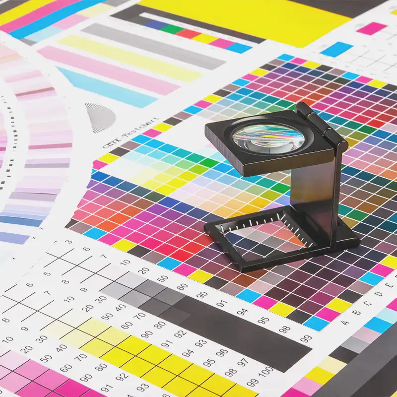 Precision in print design: A close-up of a magnifying loupe on CMYK color proofs and test charts, showcasing Artmedia Digital's commitment to high-quality print materials.