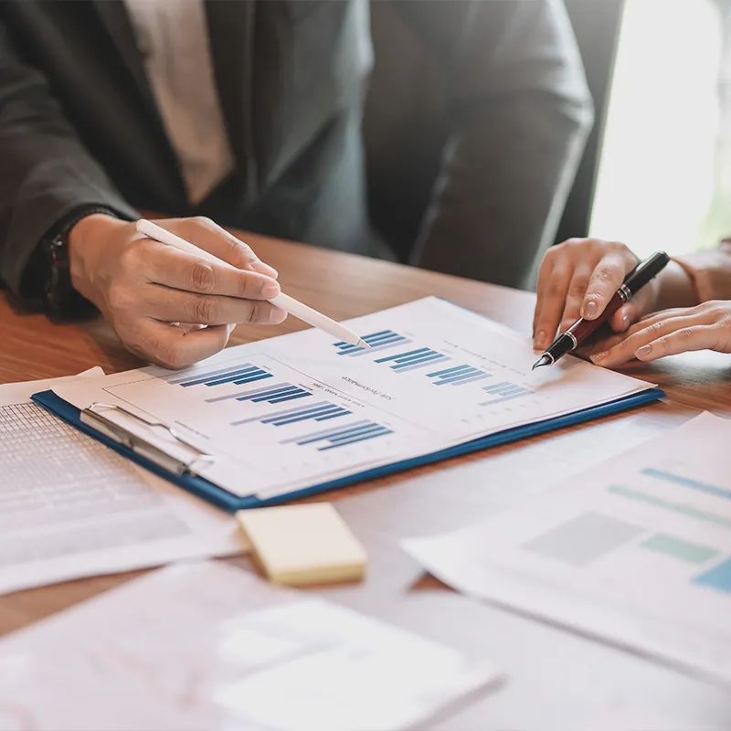 Two people discussing a bar graph on a report, symbolizing SEO (Search Engine Optimization) strategy and analysis.